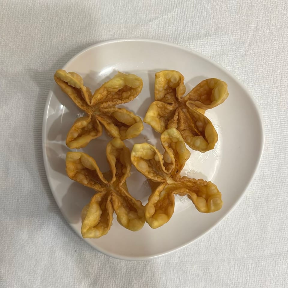 Golden fried wontons arranged on a white plate atop a textured white tablecloth.