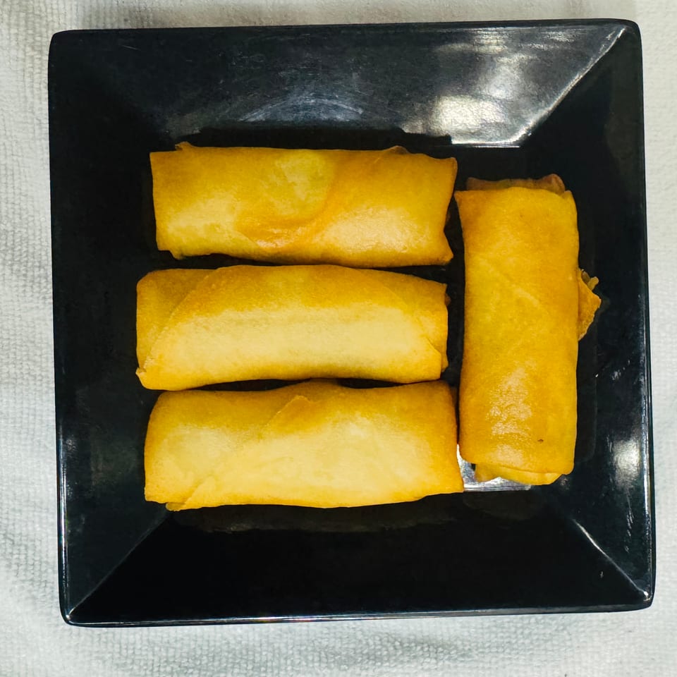 Four golden fried spring rolls arranged on a glossy black square plate atop a white textured tablecloth.